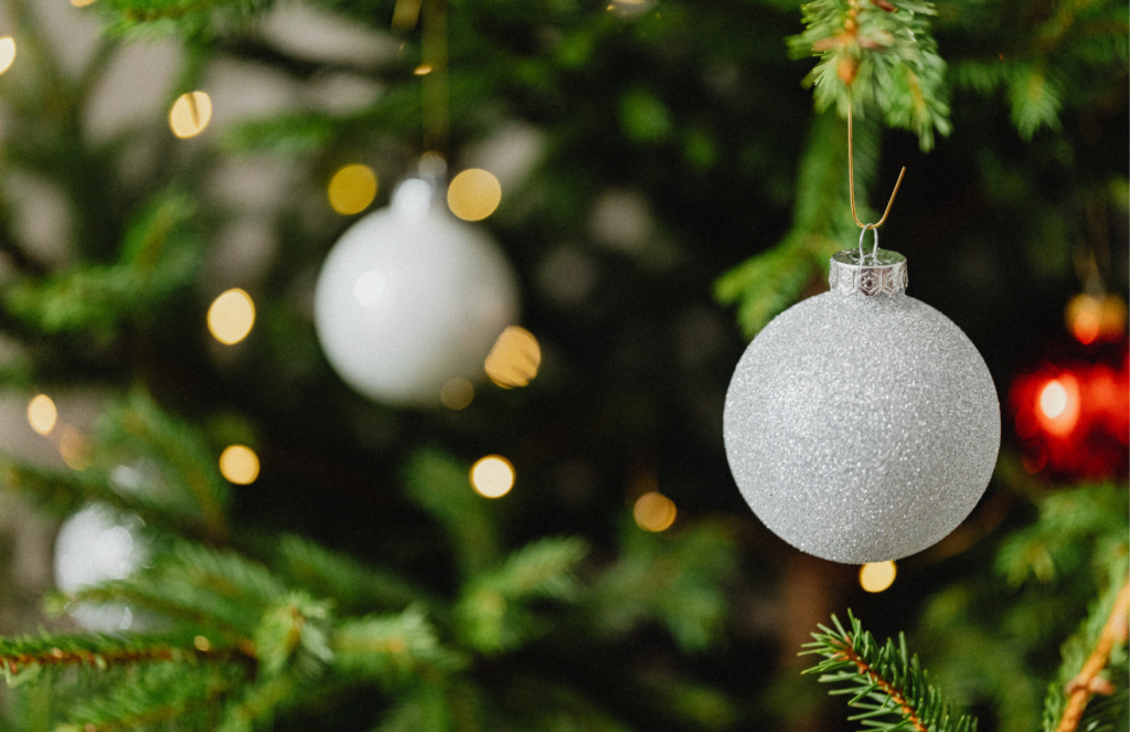 Ein Weihnachtsbaum mit weißen Kugeln und gelben Lichtern. Die Kugel im Vordergrund ist scharf fokussiert.